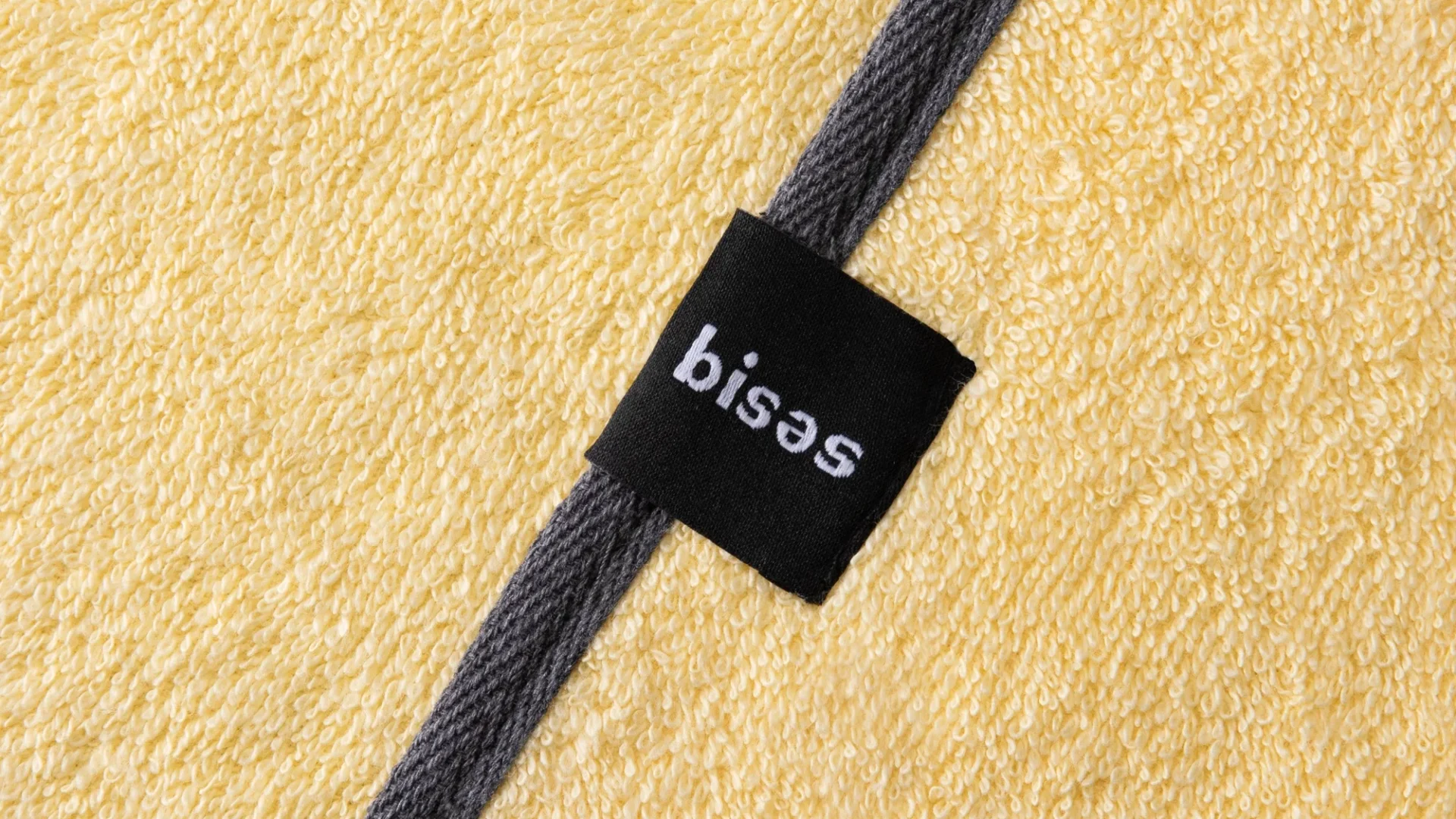 Деталь рушника Bises Nature у жовтому відтінку з темною окантовкою та логотипом