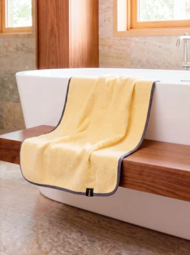 Рушник Bises Nature Bath у відтінку Butter Yellow з контрастною темною окантовкою на дерев’яній лаві біля ванни