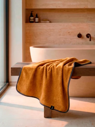 Рушник Bises Nature Bath у відтінку Mustard з контрастною темною окантовкою на дерев’яній лаві у ванній кімнаті