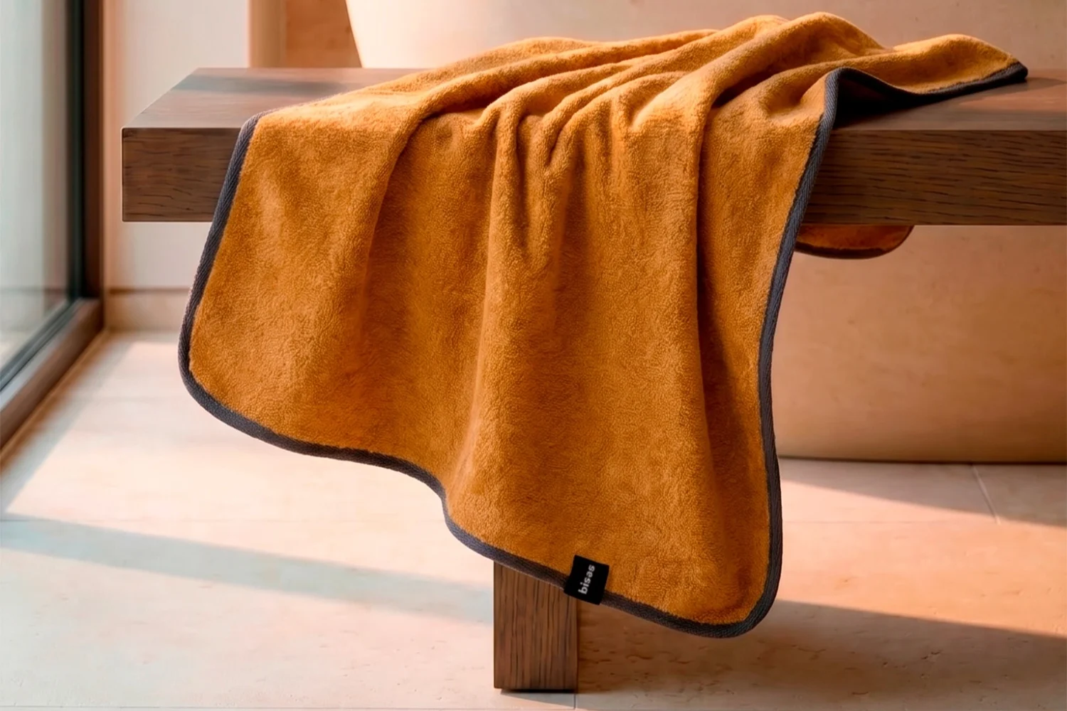 Рушник Bises Nature Bath у відтінку Mustard з контрастною темною окантовкою на дерев’яній лаві у ванній кімнаті